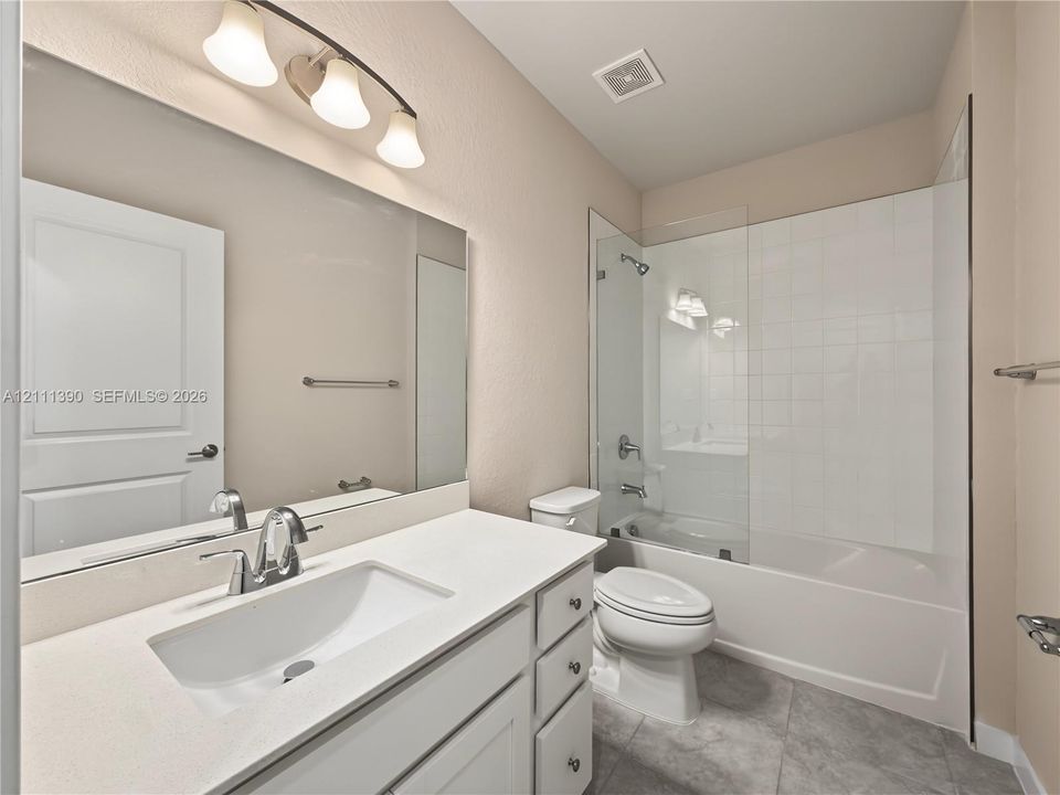 Bathroom featuring a vanity with a white countertop and rectangular undermount sink, expansive wall-to-wall mirror, glass shower door, and tile-surround tub