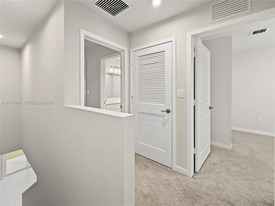 Neutral-toned interior featuring wall-to-wall carpeting, white paneled interior doors, and a louvered closet door