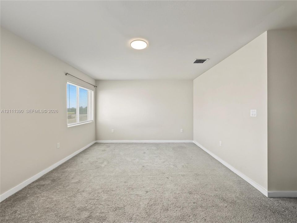 Neutral-toned interior space featuring light-colored wall paint, plush carpeting, and a single-pane window