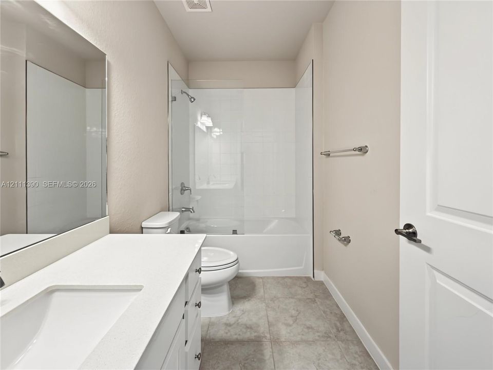 Bathroom featuring a vanity with a white countertop and rectangular undermount sink, a large wall-mounted mirror, tile flooring, and a tub-shower combination with a glass panel
