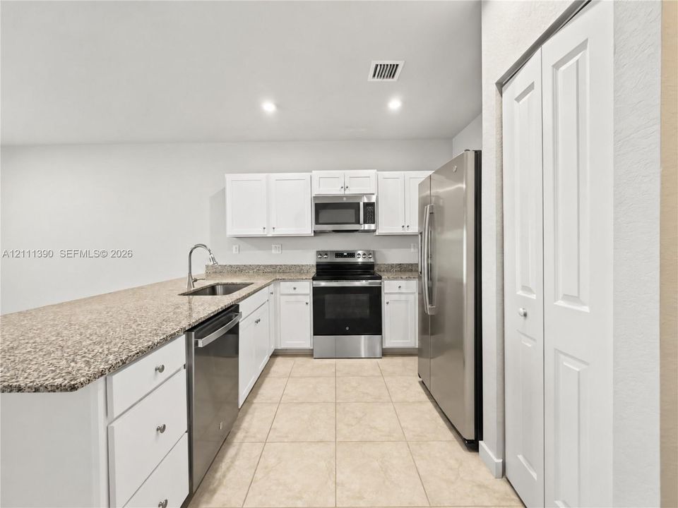 Kitchen featuring white shaker-style cabinetry, stone-finish countertops, stainless steel appliances, ceramic tile flooring, and a double-door pantry