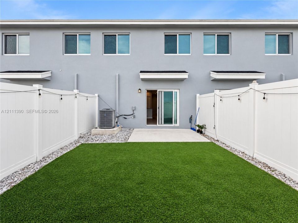 Private backyard featuring synthetic turf, concrete patio, white vinyl privacy fencing, and exterior sliding glass door