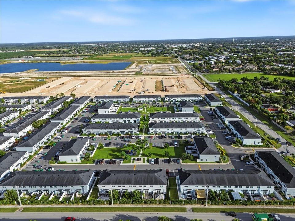 Aerial perspective of a townhome community featuring multi-family residential structures with dark shingled roofs, dedicated surface parking, manicured common green spaces, and perimeter landscaping