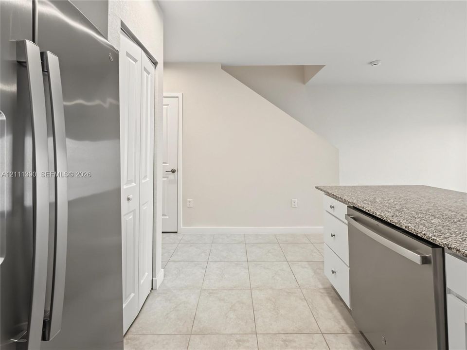 Stainless steel refrigerator, built-in dishwasher with stone-finish countertop, white shaker-style cabinetry, and ceramic tile flooring