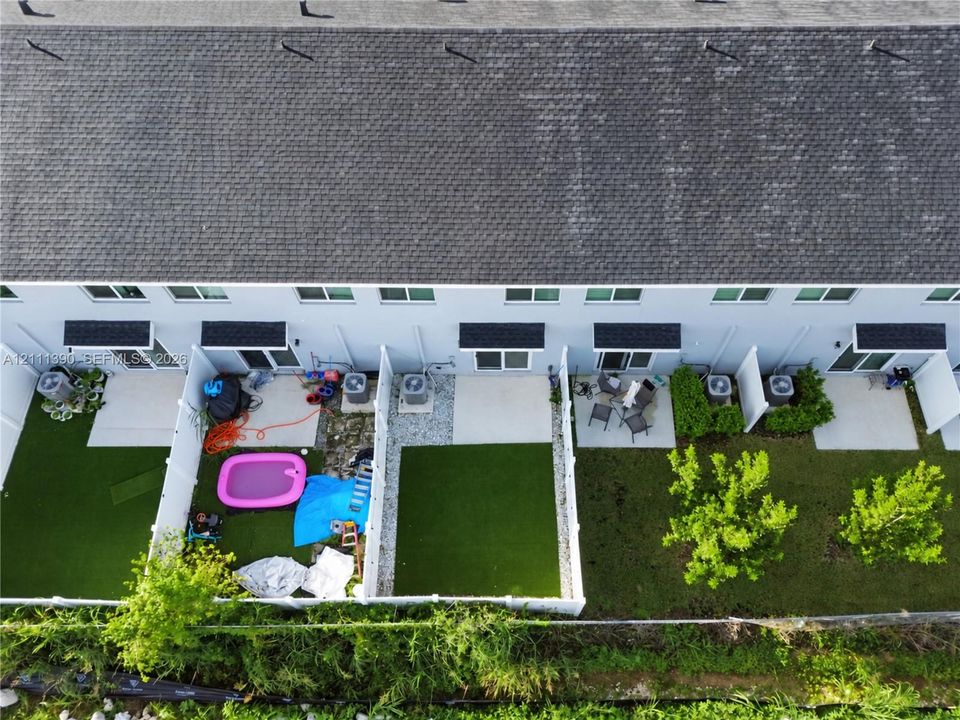 Aerial perspective of townhome exteriors featuring low-maintenance artificial turf lawns, concrete patios, and white vinyl privacy fencing
