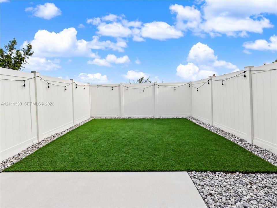 Enclosed backyard featuring a white vinyl privacy fence, synthetic turf lawn, concrete patio, and gravel borders
