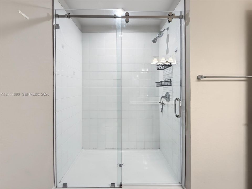 Walk-in shower featuring white subway wall tile, a frameless glass sliding door with brushed metal hardware, and a fixed shower head