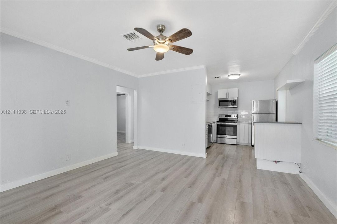 Wood-finish flooring, central ceiling fan with integrated lighting, and kitchen featuring stainless steel appliances, crisp white cabinetry, and a peninsula counter