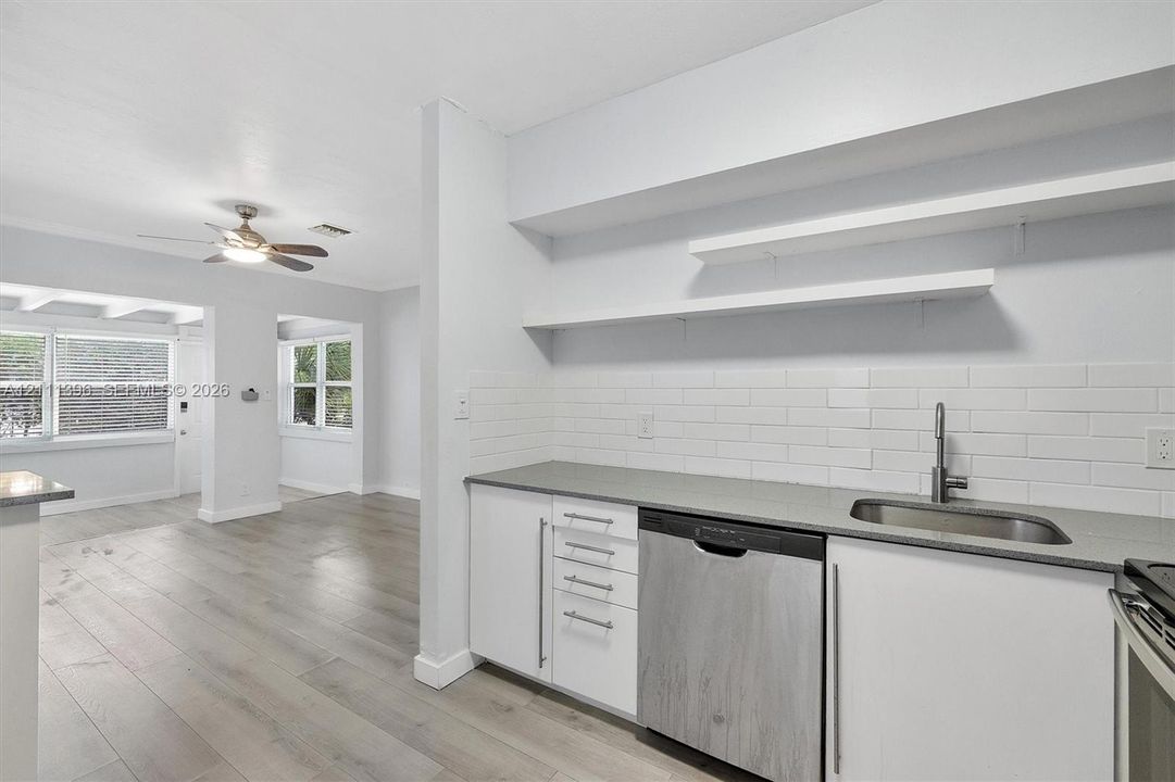 Kitchen featuring white flat-panel cabinetry, light-toned countertops, subway tile backsplash, stainless steel dishwasher, and open shelving