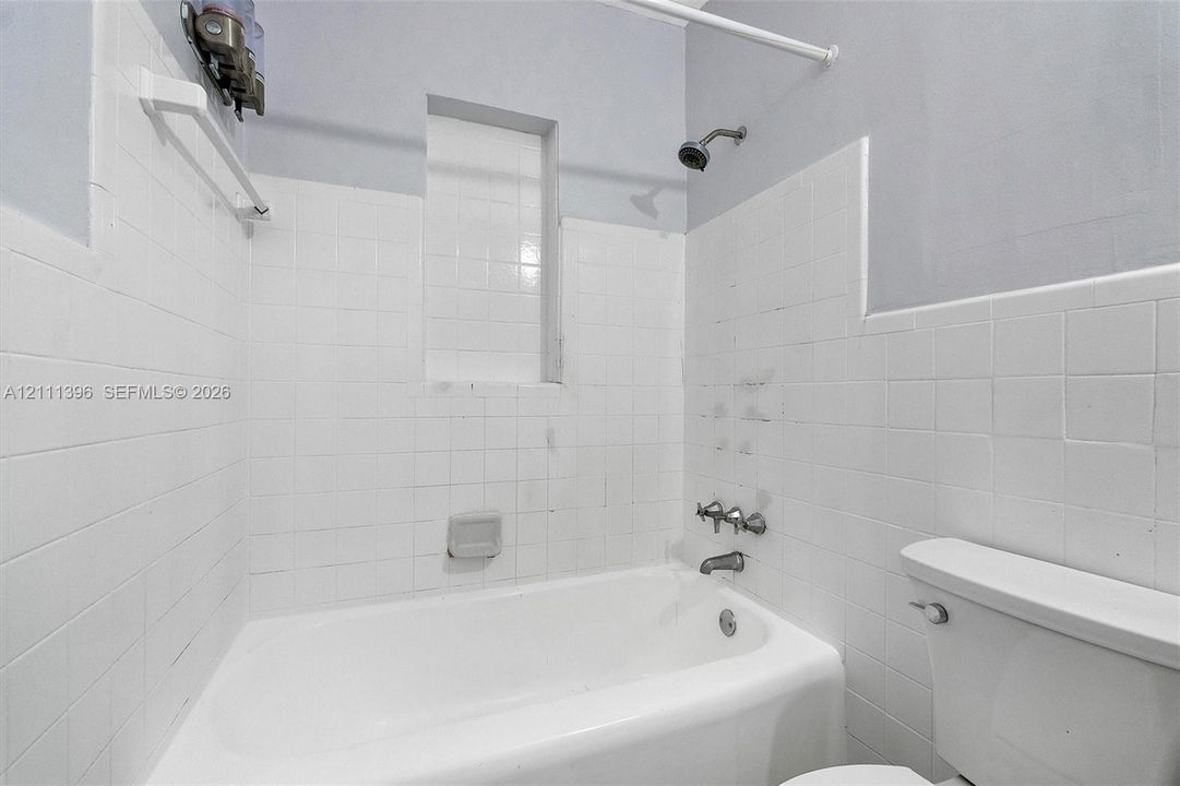 Bathroom featuring a white porcelain tub, ceramic wall tiling, a built-in recessed shelf, and a dual-handle metal faucet