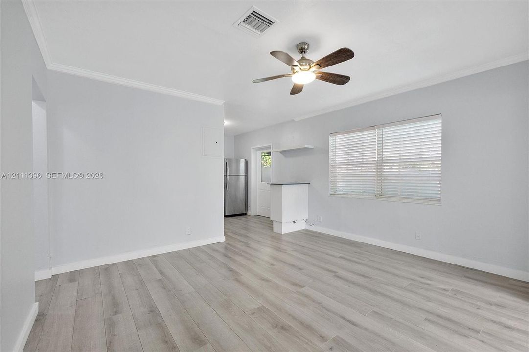 Neutral-toned room featuring wood-finish flooring, a ceiling-mounted fan with integrated lighting, horizontal window blinds, and a built-in counter surface