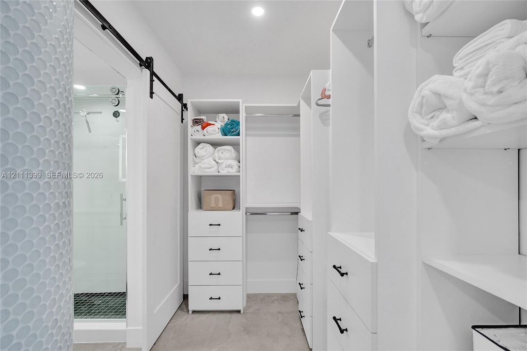 Walk-in closet featuring white built-in cabinetry, custom shelving, multiple drawers with matte black hardware, and a sliding barn-style door