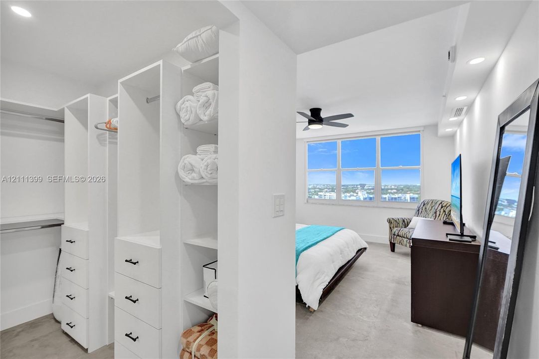 Custom walk-in closet featuring white built-in shelving, hanging rods, and drawers with matte black hardware, recessed ceiling lighting, and large windows with exterior scenery