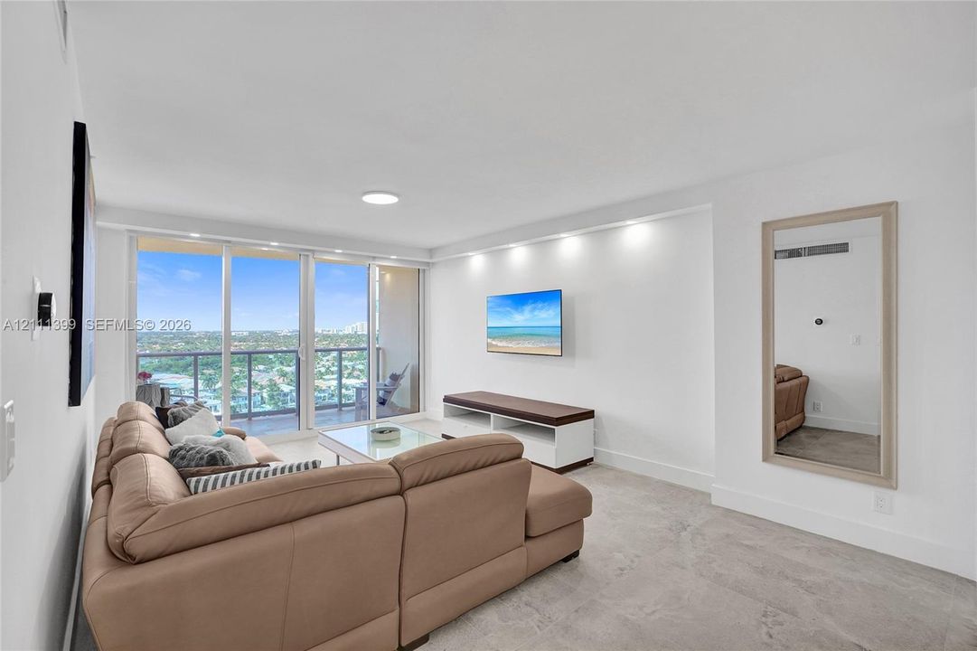 Living area featuring neutral stone flooring, floor-to-ceiling glass sliding doors, recessed lighting, and a private balcony with an expansive exterior outlook