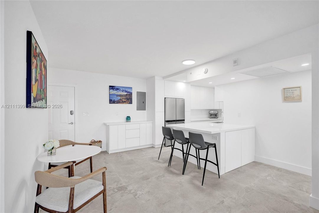 Modern kitchen featuring a central island with integrated storage, flat-panel cabinetry, light-toned stone-finish countertops, stainless steel appliances, and large-format tile flooring
