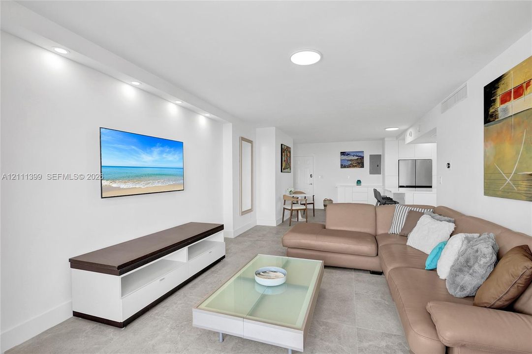 Open-concept living area featuring light-toned tile flooring, recessed ceiling lighting, and a custom built-in media console with storage