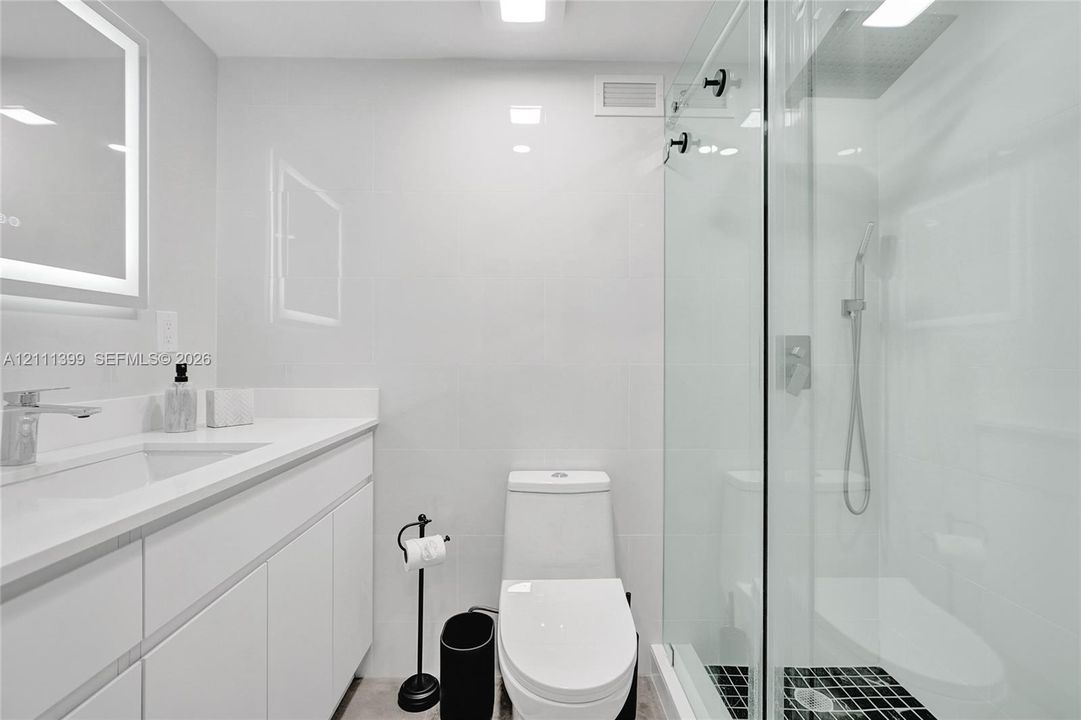 Bathroom featuring a glass-enclosed walk-in shower with a rainfall showerhead, white vanity with integrated basin, polished metal hardware, and LED-backlit mirror