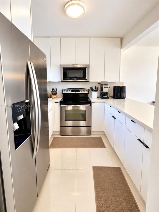 Kitchen featuring white cabinetry, solid-surface countertops, tile flooring, and stainless steel appliances including a built-in microwave and refrigerator