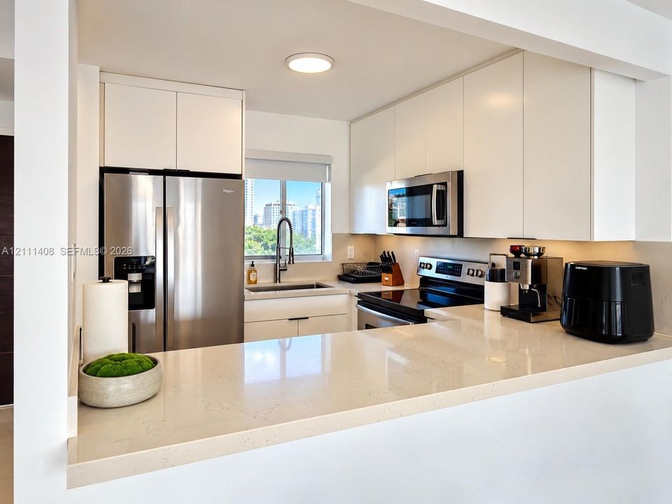 Kitchen featuring flat-panel white cabinetry, solid-surface countertops with a breakfast bar, stainless steel appliances, and a single-basin undermount sink with a gooseneck faucet