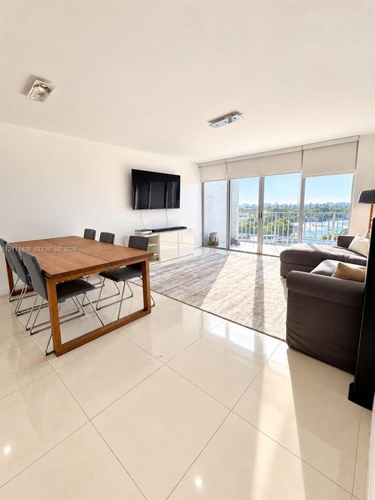 Large-format tile flooring, recessed ceiling lighting, and floor-to-ceiling glass sliding doors opening to a balcony with waterfront and city scenery