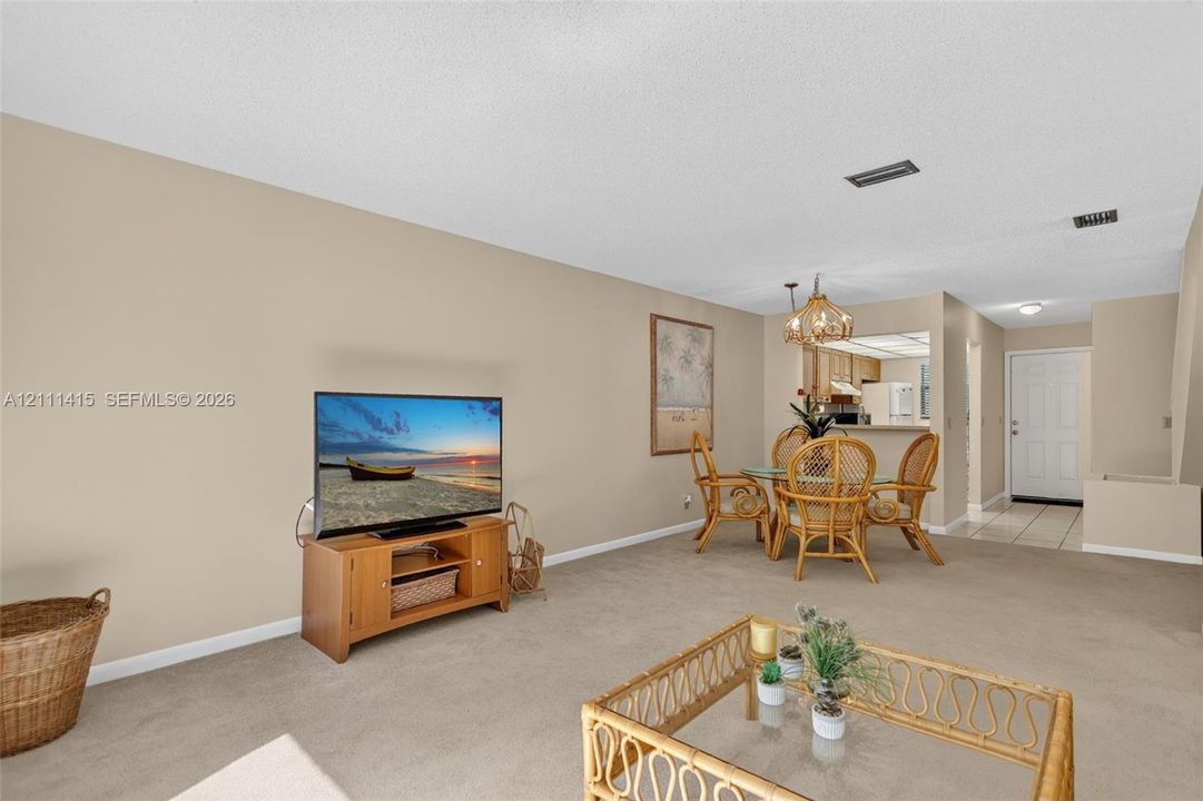 Open-concept main living area featuring neutral wall paint, wall-to-wall carpeting, a decorative multi-bulb chandelier, and a pass-through kitchen opening