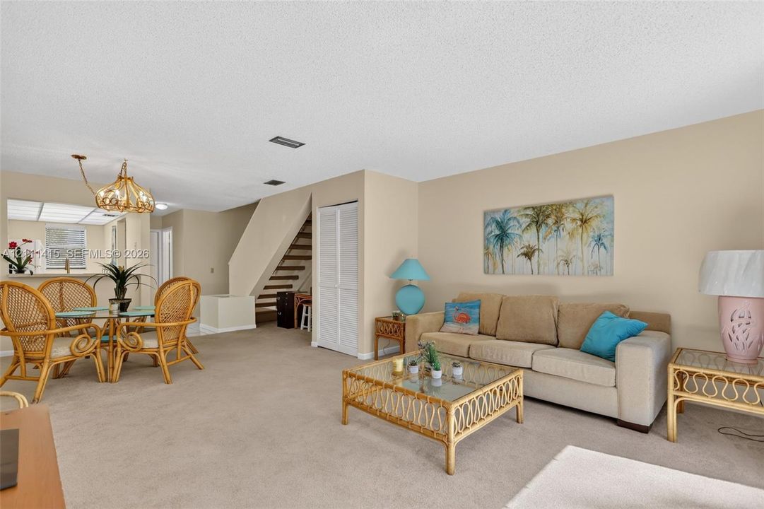 Open-concept floor plan featuring neutral wall finishes, wall-to-wall carpeting, a multi-tiered staircase with open risers, and a decorative pendant light fixture