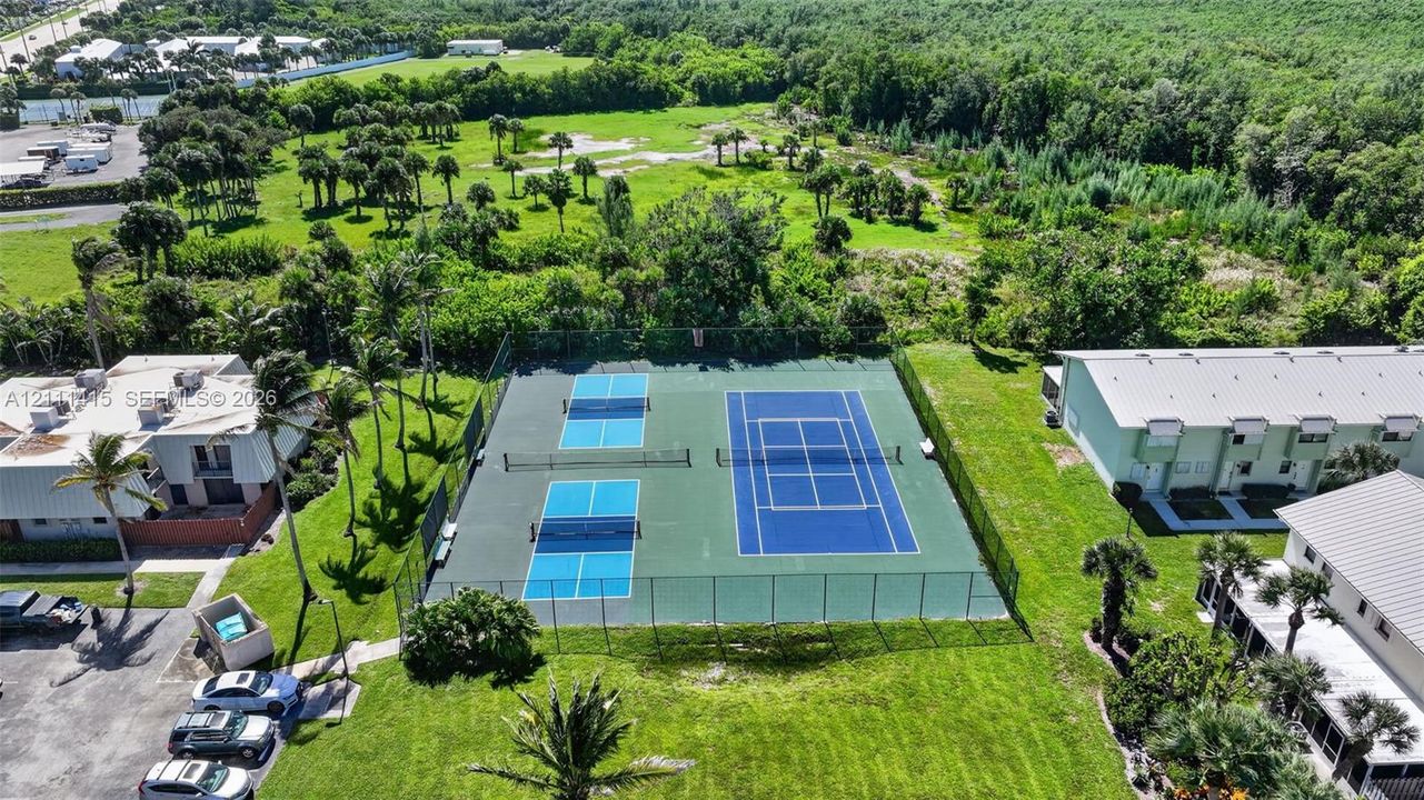 Fenced recreation area featuring a tennis court and two pickleball courts with perimeter chain-link enclosures
