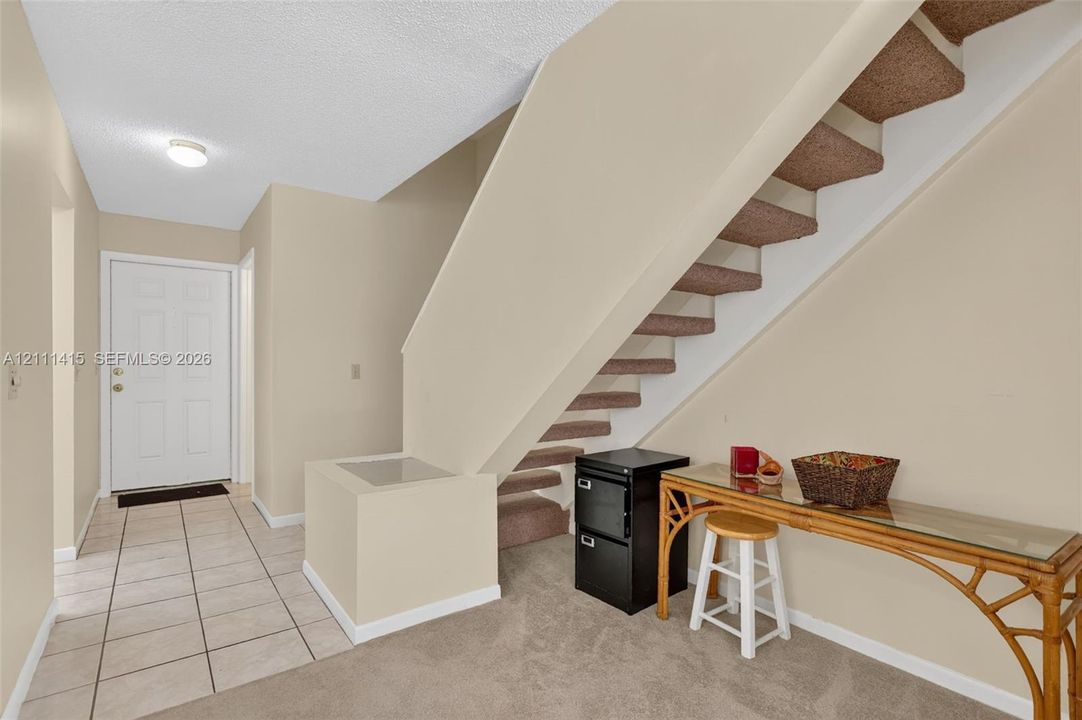 Foyer featuring neutral-toned tile flooring, carpeted staircase with enclosed structural balustrade, and a recessed ceiling light fixture