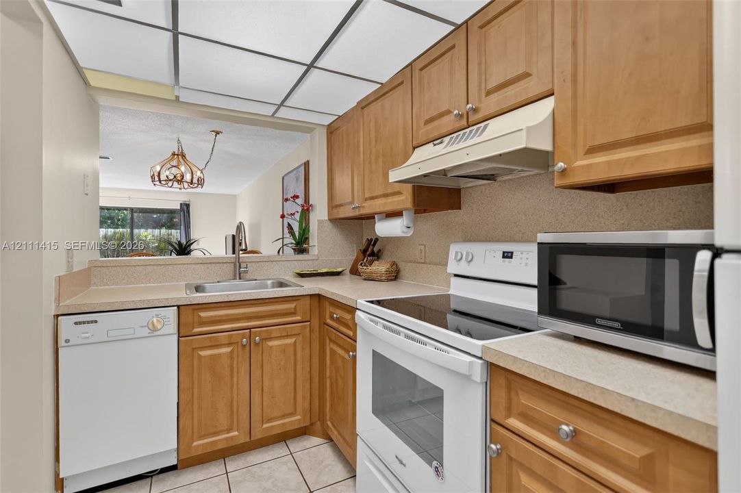 Kitchen featuring shaker-style wood cabinetry, solid-surface countertops, a drop-in stainless steel sink, and a grid-pattern drop ceiling