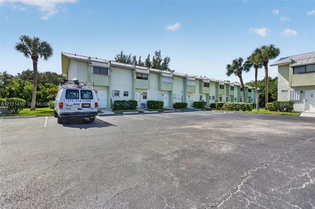 Multi-unit residential complex featuring light-toned siding, metal roofing, individual entryways, and palm tree landscaping