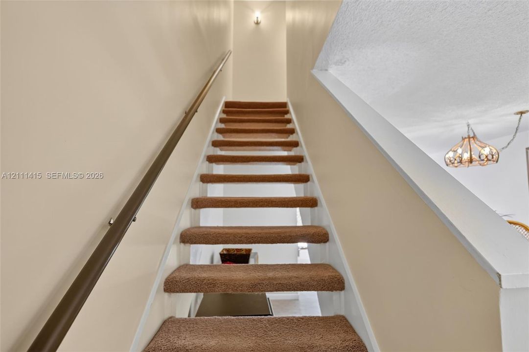 Staircase featuring wall-to-wall carpeted treads, a solid wood handrail with metallic mounting hardware, and a semi-flush mount ceiling light fixture