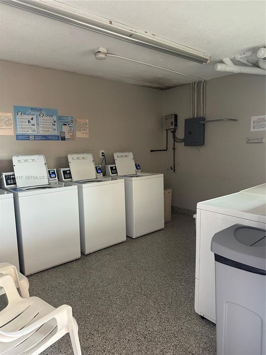 Laundry room featuring multiple high-capacity top-load washing machines and durable epoxy flooring