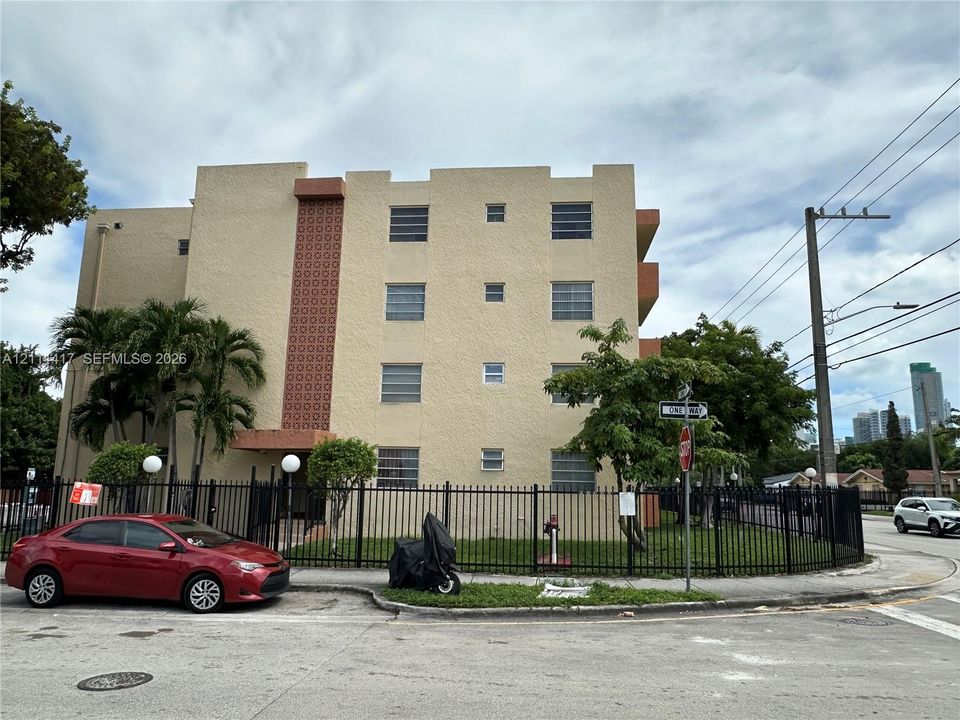 Multi-story residential building exterior featuring stucco cladding, decorative geometric masonry accents, jalousie windows, and a perimeter metal fence