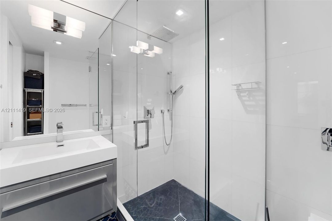 Glass-enclosed walk-in shower with stone tile flooring, modern wall-mounted faucet, rectangular integrated sink, and polished chrome hardware