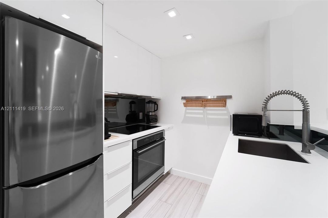 Kitchen featuring high-gloss white cabinetry, quartz countertops, a stainless steel refrigerator, an integrated cooktop with a built-in oven, and a gooseneck faucet
