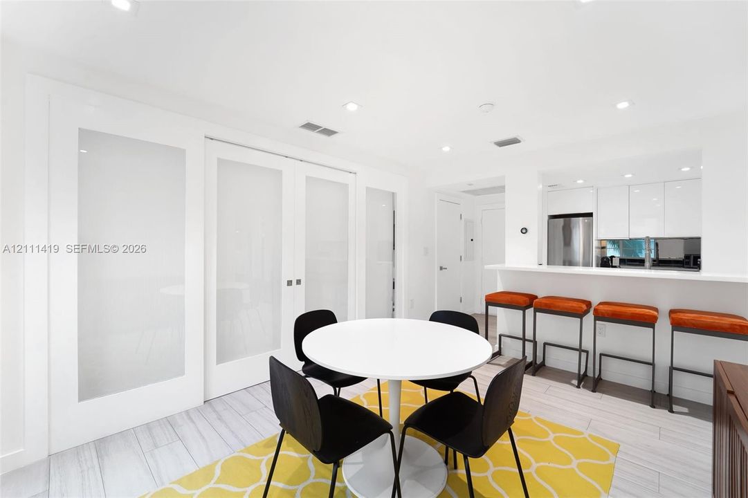 Interior space featuring white high-gloss cabinetry, breakfast bar with integrated counter, wood-finish tile flooring, and frosted glass paneled doors with white frames