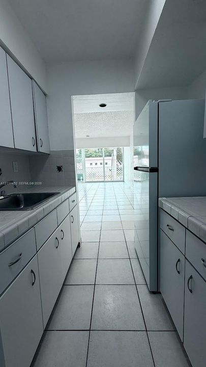 Galley-style kitchen featuring white cabinetry, tile countertops, stainless steel sink, and ceramic tile flooring