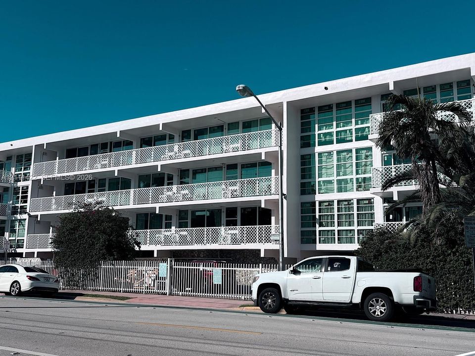 Multi-story facade featuring white structural concrete, expansive floor-to-ceiling glass windows, and private balconies with decorative geometric railings