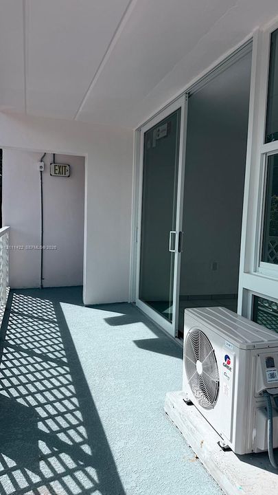 Covered balcony featuring a white metal railing, large sliding glass door, and a wall-mounted exterior HVAC unit