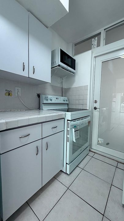 Kitchen featuring white cabinetry, ceramic tile countertops, light-colored tile flooring, integrated electric range, and a full-lite glass door