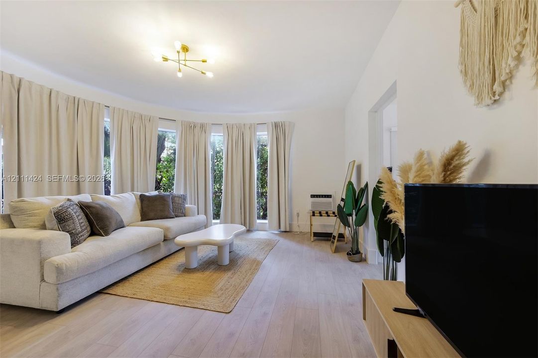 Living space featuring wood-finish flooring, a semi-circular bay window, and a multi-arm geometric ceiling light fixture