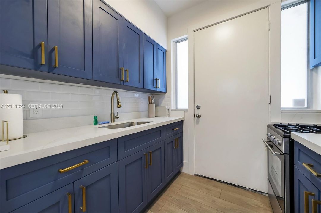 Kitchen featuring navy blue Shaker-style cabinetry, matte gold hardware, white subway tile backsplash, solid-surface countertops, and wood-finish flooring