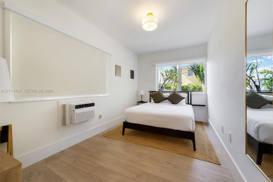 Room featuring wood-finish flooring, a wall-mounted climate control unit, a recessed window, a flush-mount globe light fixture, and a full-length wall mirror