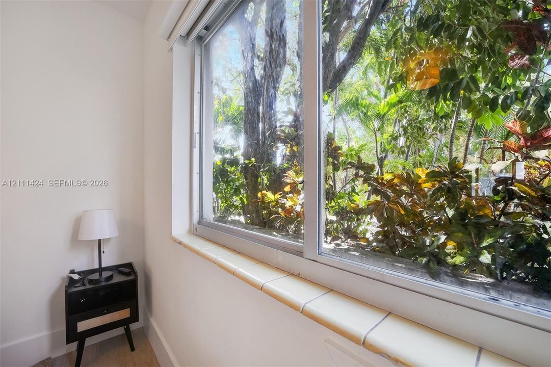 Large sliding window with a tiled sill, featuring white walls and exterior tropical foliage