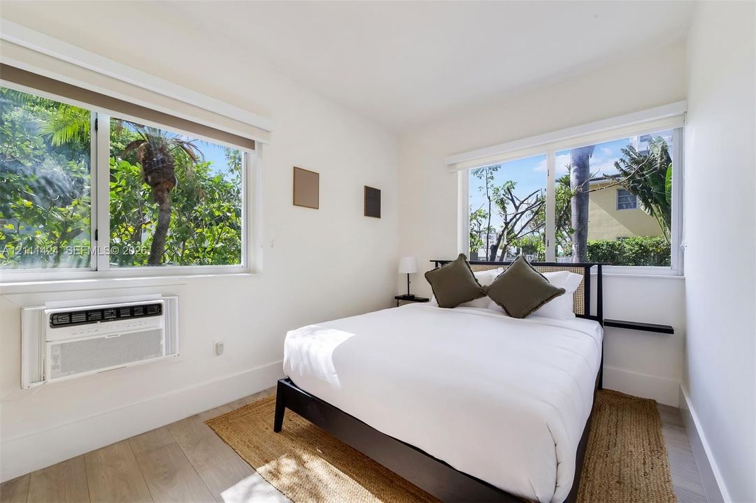 Bright room featuring wood-finish flooring, dual-aspect windows, and a wall-mounted air conditioning unit
