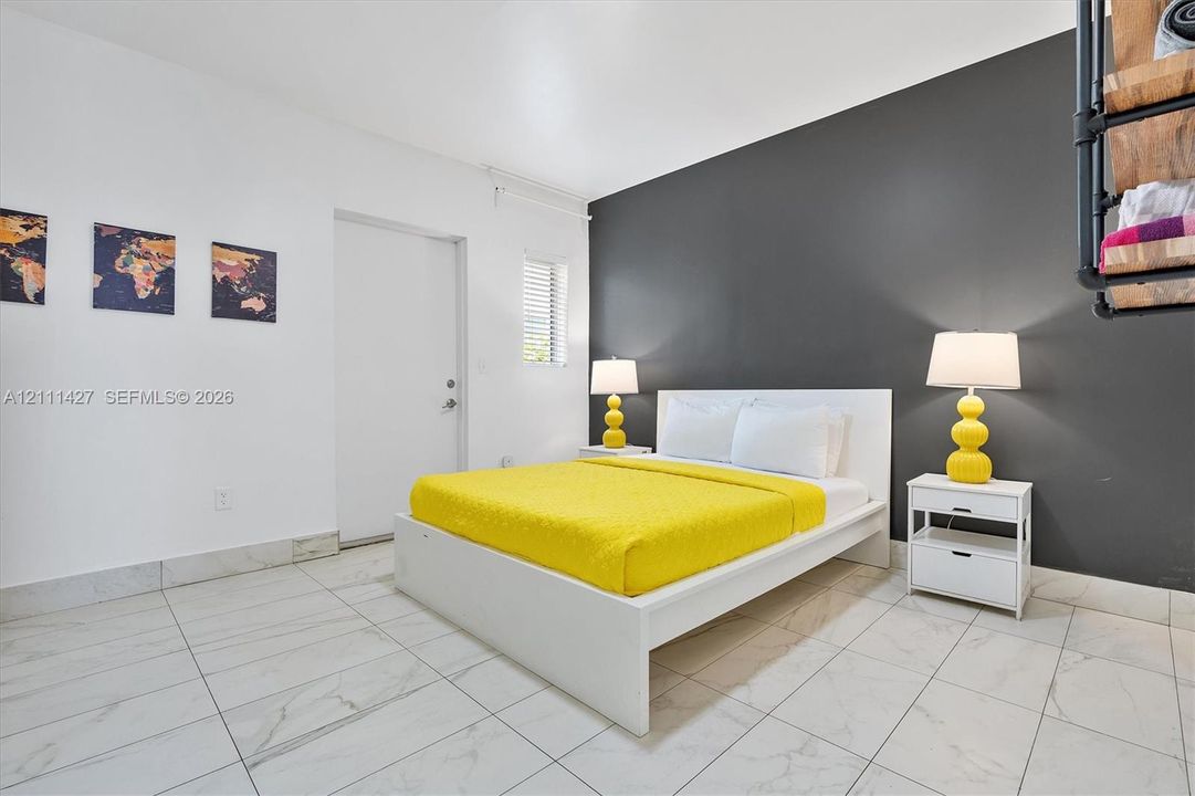 Room featuring large-format stone-patterned tile flooring, a charcoal-toned accent wall, and a horizontal louvered window