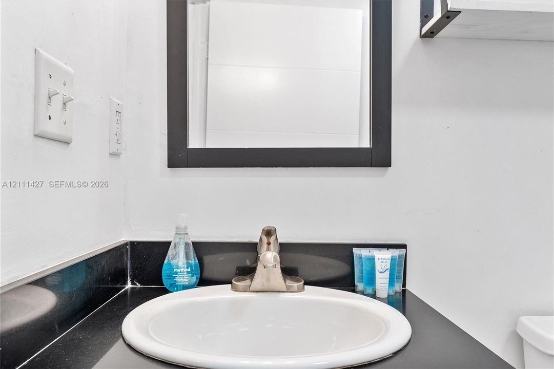 Bathroom vanity featuring a dark solid-surface countertop, an integrated white oval sink, and a high-arch metal faucet, accented by a black-framed wall mirror