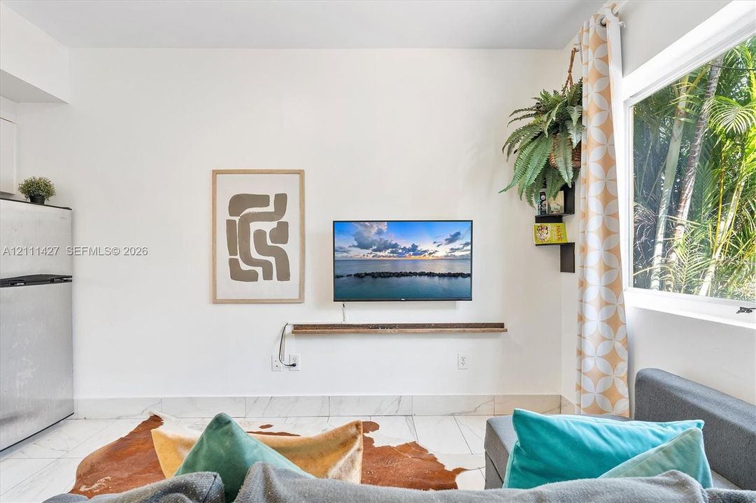 Large window, stone-finish tile flooring, and wall-mounted wooden shelf