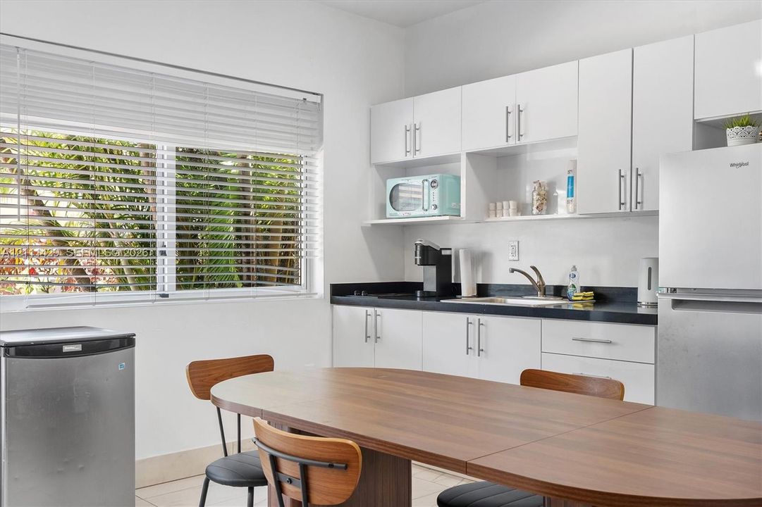 Kitchen featuring white cabinetry, dark stone-finish countertops, stainless steel refrigerator, and horizontal blind-covered windows