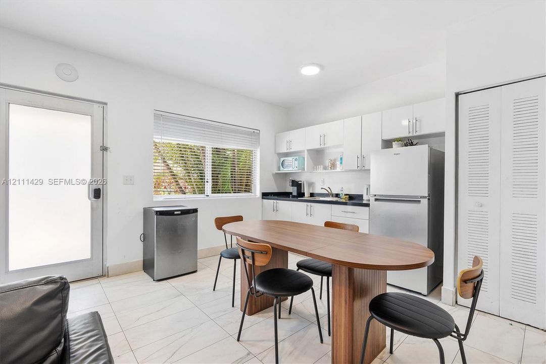 Kitchenette featuring white cabinetry, contrasting dark countertops, a stainless steel refrigerator, white tile flooring and a closet with louvered doors